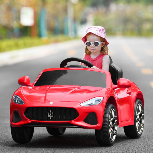 A young child wearing a pink hat driving the red electric ride on car on a road