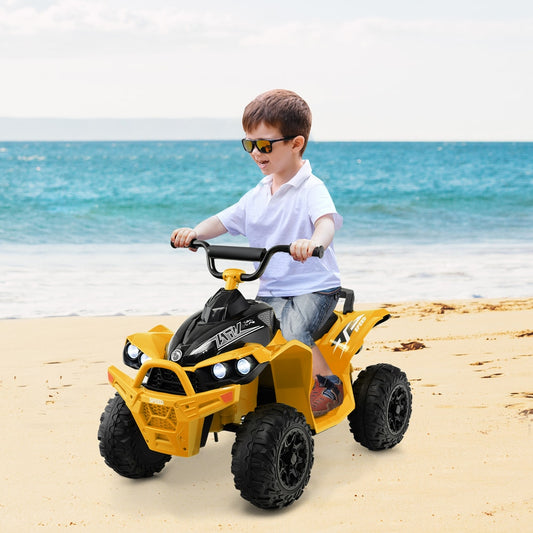 A young boy rides the yellow kids electric quad bike on a sandy beach