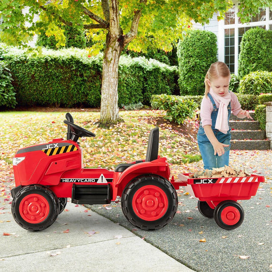 A young girl stands next to the red ride on tractor with trailer in a garden
