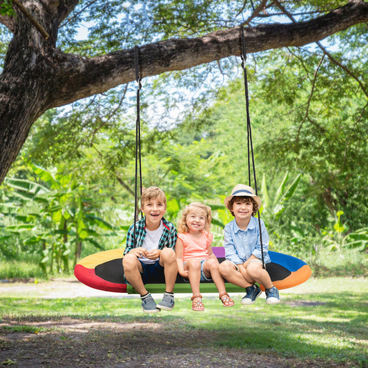 Three children sitting on the oval swing suspended from a tree branch in a garden