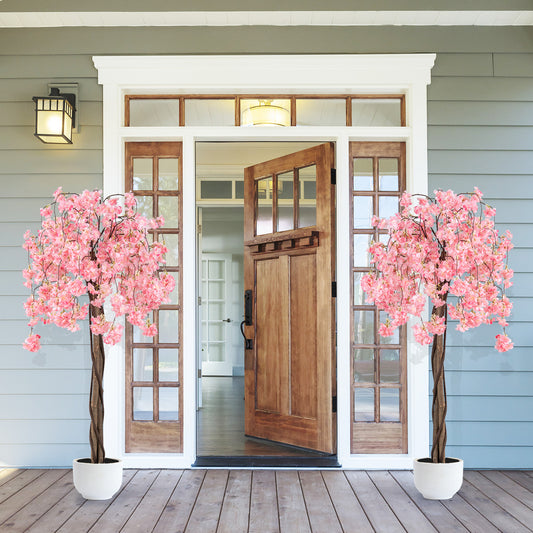 Two faux plants with pink cherry blossoms standing in white pots on a wooden porch