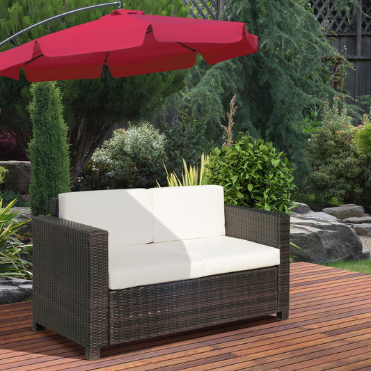 The rattan furniture placed on a wooden patio under a red parasol in a garden