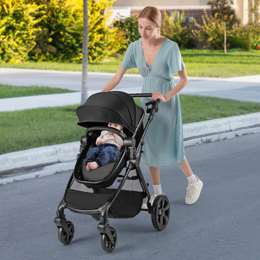 The baby stroller being pushed by a woman on a paved path with a baby sitting inside