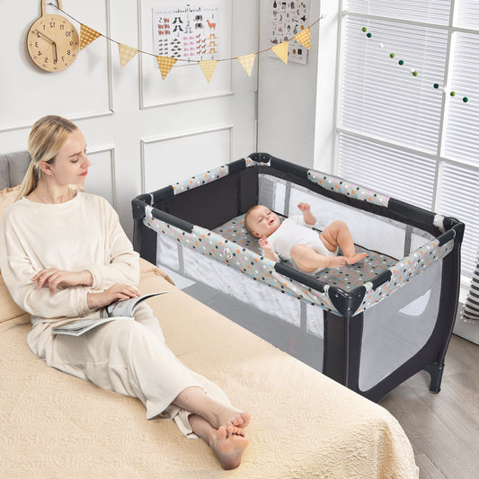 Woman reading on bed next to the grey baby playpen with a baby inside