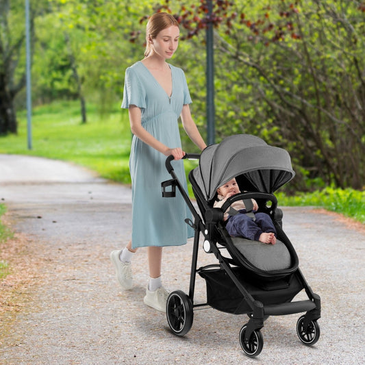 Woman pushing a grey high landscape stroller with a baby inside on a path