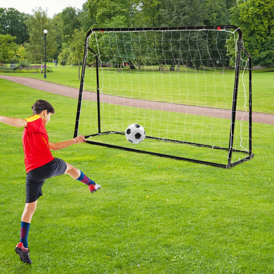 Young boy in a red shirt kicking a soccer ball towards the soccer goal in a park
