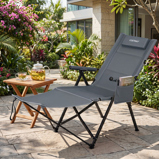 The grey camping chair is shown reclined with its footrest extended, beside a small wooden table with a teapot