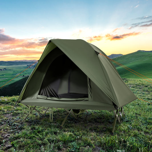 Green camping tent on a cot in a grassy field with hills in the background