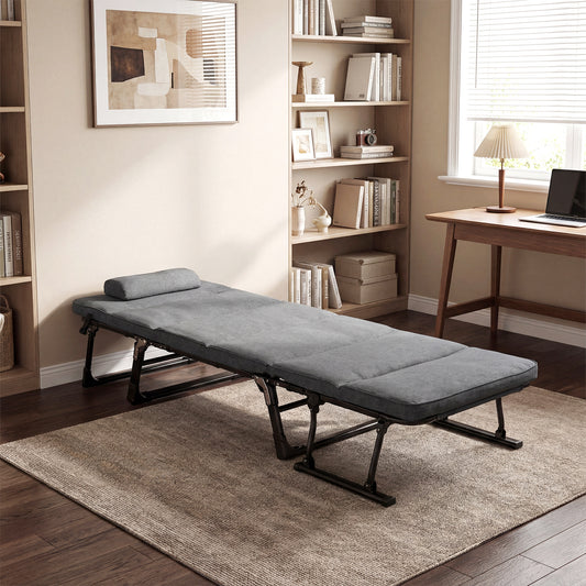 The grey camping cot set up as a bed in a living room with bookshelves and a desk