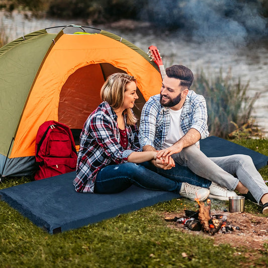 A couple sitting on two navy sleeping pads by a tent and campfire
