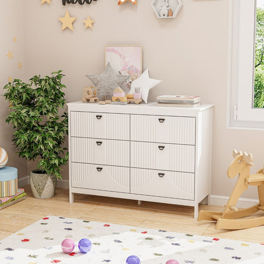 A white six-drawer dresser with black handles in a child's bedroom
