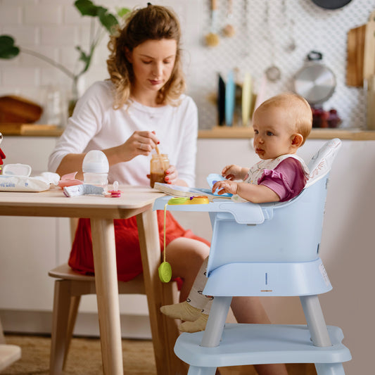 A woman feeding a baby in the blue high chair at a kitchen table
