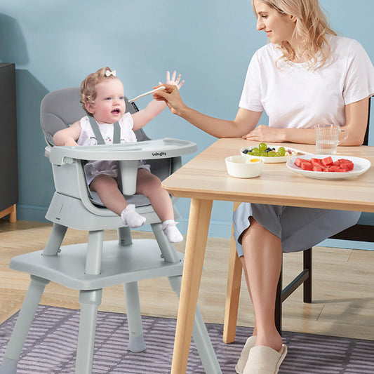 The grey high chair in use with a baby sitting at a dining table while being fed by a woman