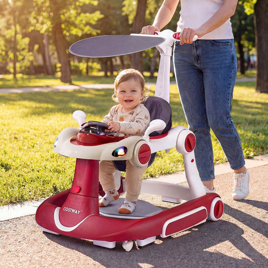 A smiling baby sits in the red baby walker push car with a canopy overhead, outdoors on a path
