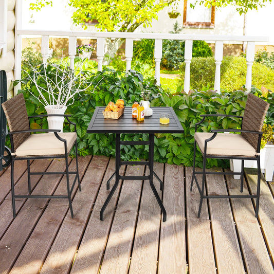 The patio table set with two wicker chairs on a wooden deck in a garden