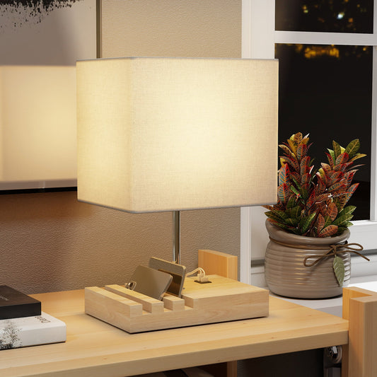 The table lamp glowing on a wooden desk next to a potted plant and books