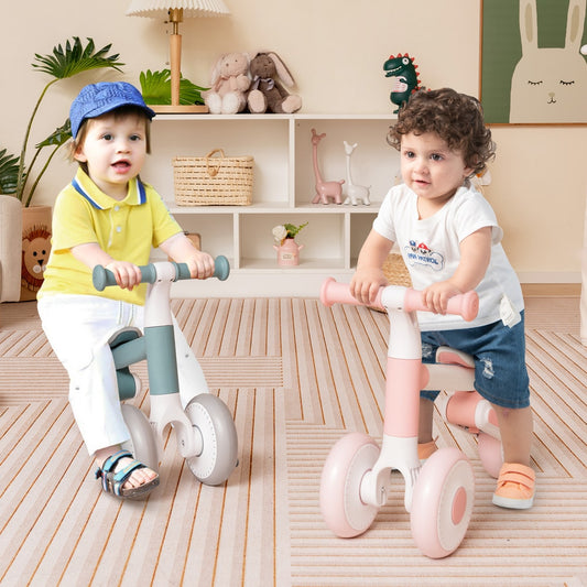 Two toddlers playing with pink and grey balance bikes indoors on a carpeted floor