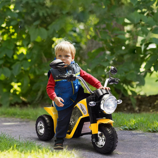 A young boy riding the yellow kids electric motorbike on a paved path outdoors with green foliage in the background