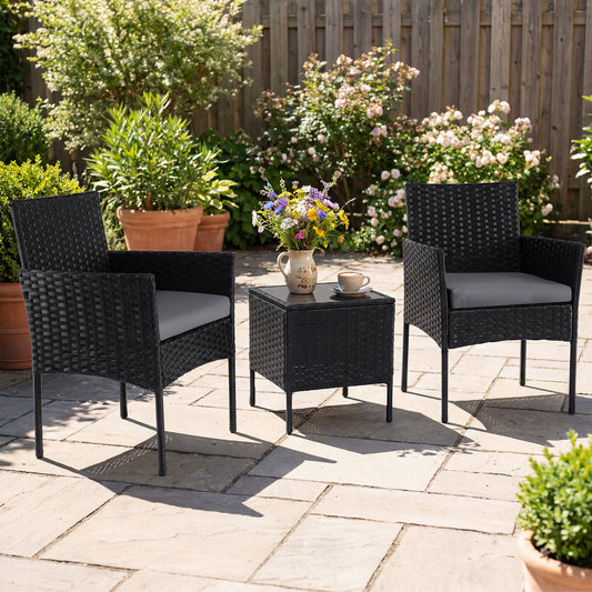 Two grey cushioned chairs and a coffee table on a paved patio with plants
