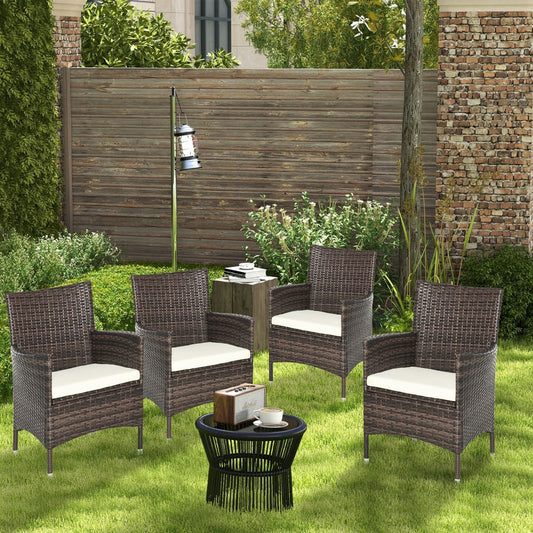 Four rattan chairs with cream cushions around a small black table in a garden setting