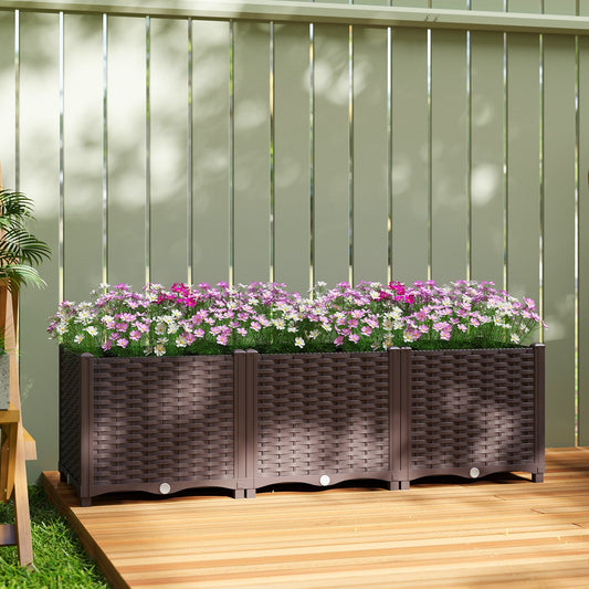 A long brown planter with a woven texture on legs filled with pink flowers, sitting on a wooden deck