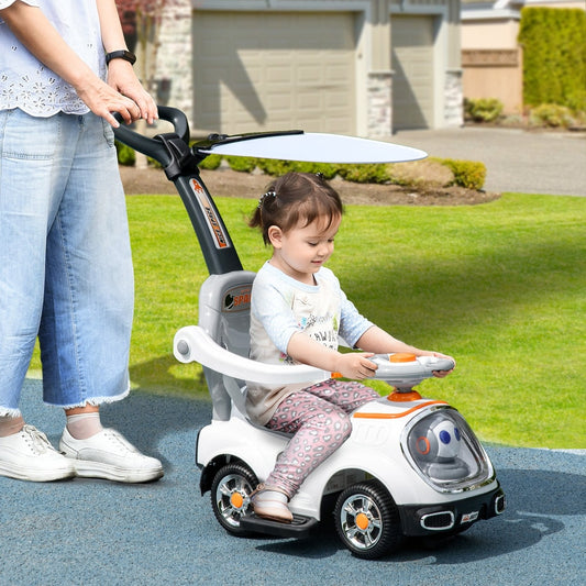 A toddler sits on the white cartoon robot ride on push car, being pushed by an adult outdoors