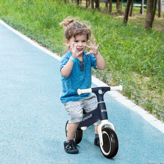 The blue baby balance bike being ridden by a child on a paved outdoor path