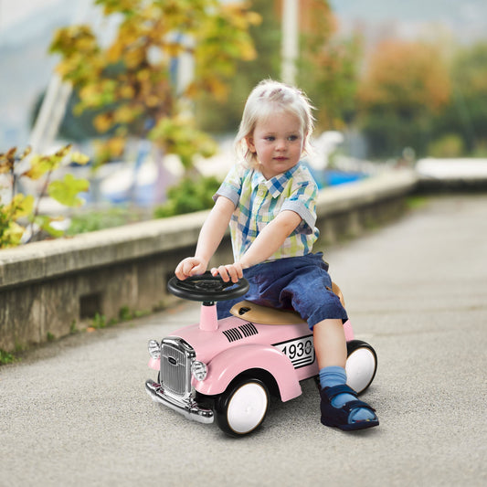 A young child sitting on the pink ride-on car and pushing it along a paved outdoor path
