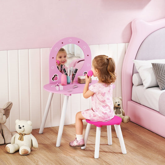A young girl sits at the pink dressing table, playing with makeup in the mirror