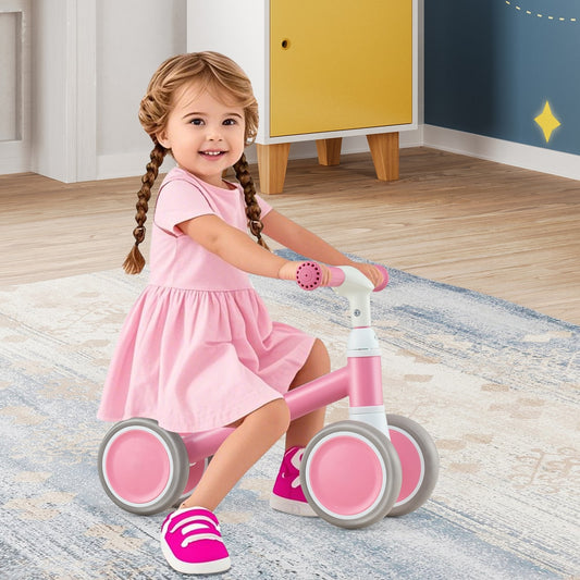 A happy toddler girl riding the pink balance bike indoors