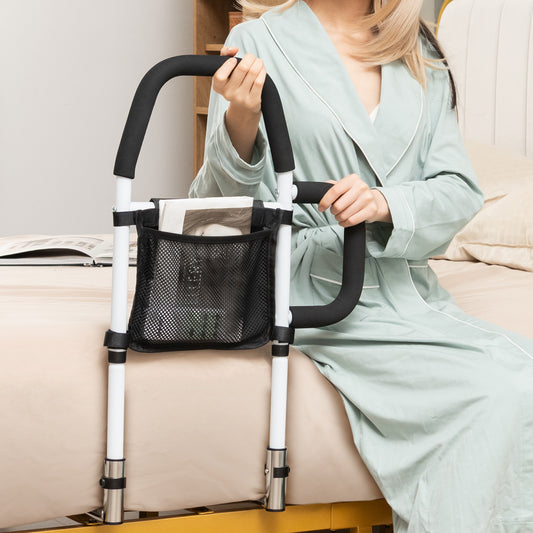 The bed rail in use with a person holding the padded handle while sitting on the edge of a bed