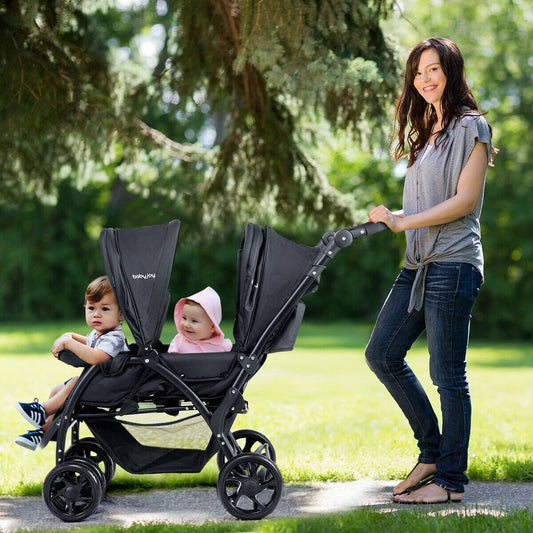 A black double pushchair with two babies being pushed by a woman in a park