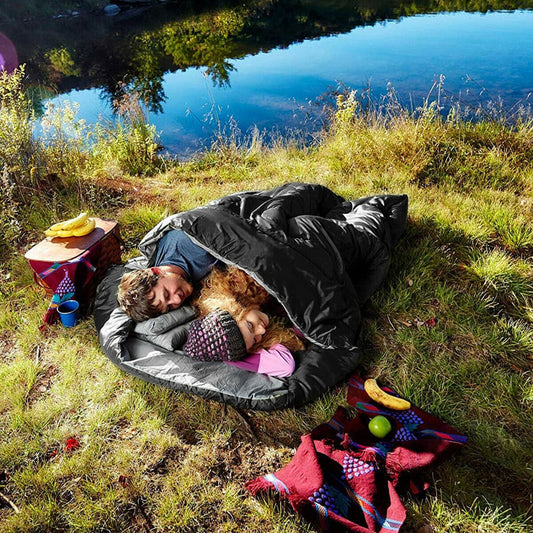 Couple sleeping in the waterproof double sleeping bag outdoors by a lake