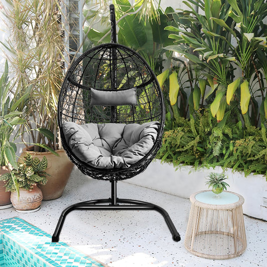 The grey egg-shaped hanging chair with stand is shown outdoors on a patio next to a pool