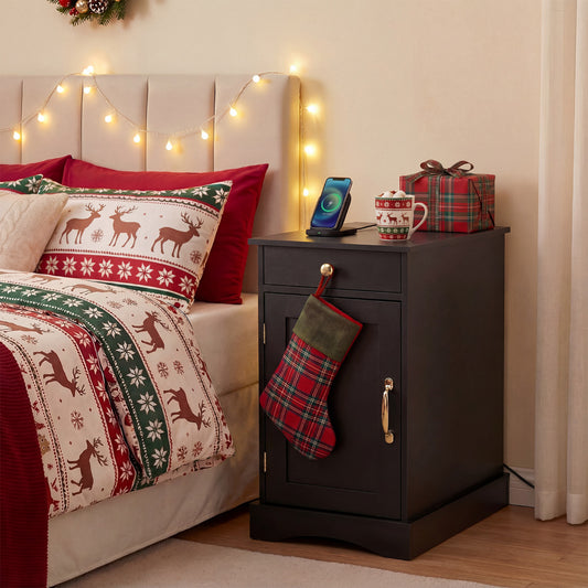 The nightstand beside a bed decorated for Christmas with a phone charging on the top surface