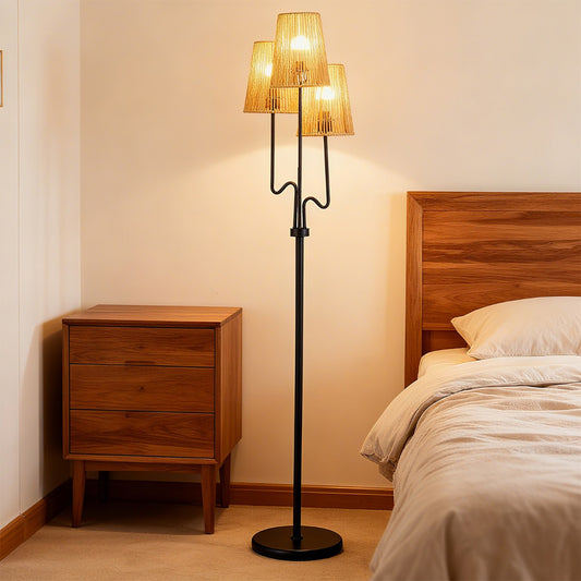 The floor lamp standing next to a wooden bedside table and a bed in a warm bedroom setting