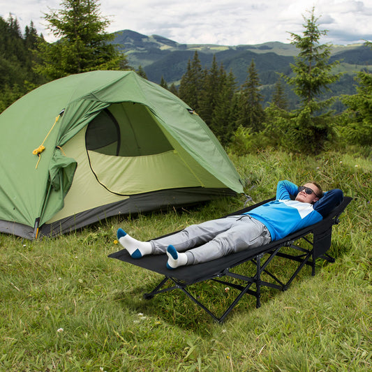 Man relaxing on the camping furniture next to a green tent in a mountainous landscape