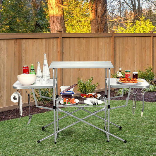 The camping furniture stands on a lawn with food and drinks arranged on its various surfaces