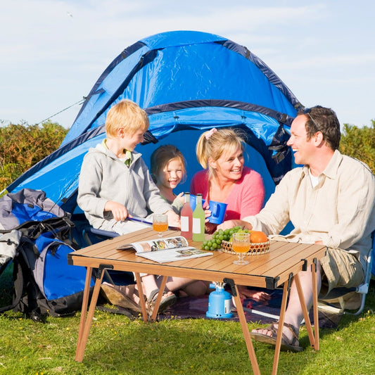 The camping furniture set up in front of a blue tent with a family having a picnic meal