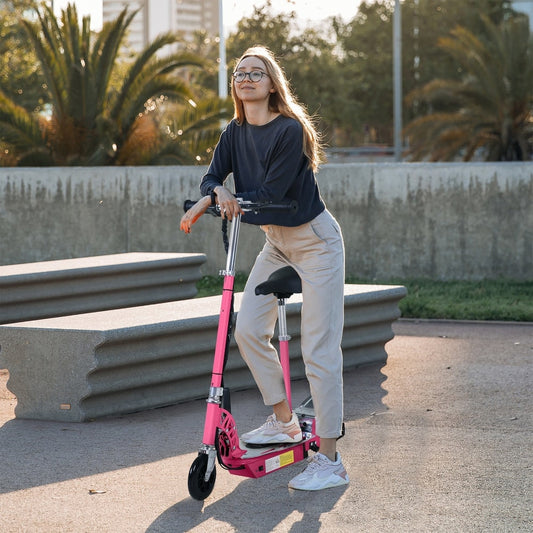 The kids scooter being used by a woman standing on the deck in a park setting