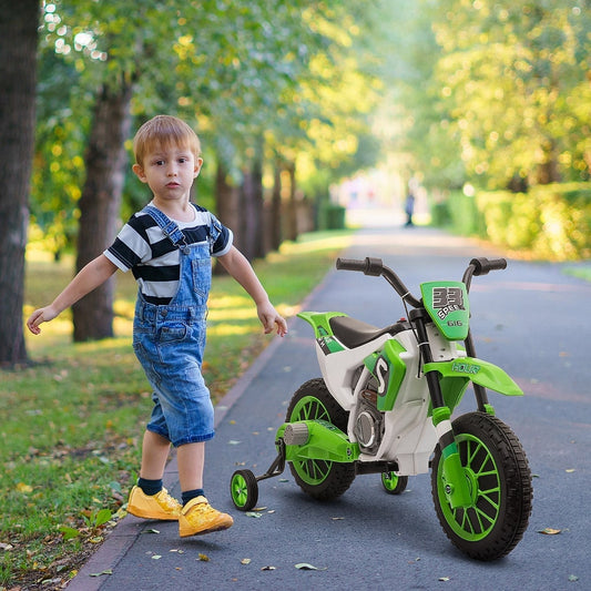 Young boy standing next to the green kids electric motorbike with training wheels on a paved path