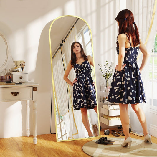 The full length mirror placed in a bright bedroom with a woman standing in front of it