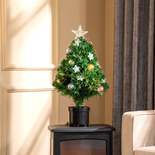 The tabletop Christmas tree is lit up and placed on a dark surface next to a curtain