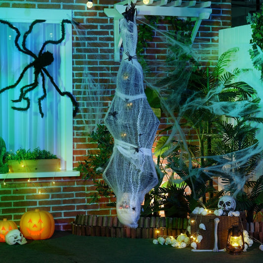 The hanging mummy decoration in a garden setting with pumpkins and spider webs