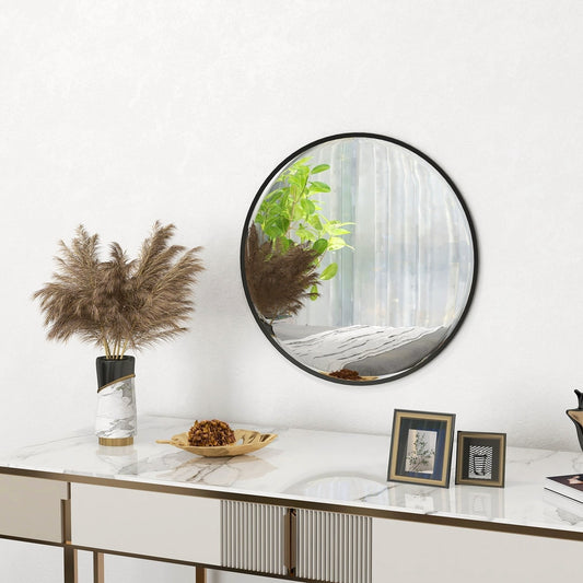 A round wall mirror with a black frame placed on a console table with decorative items