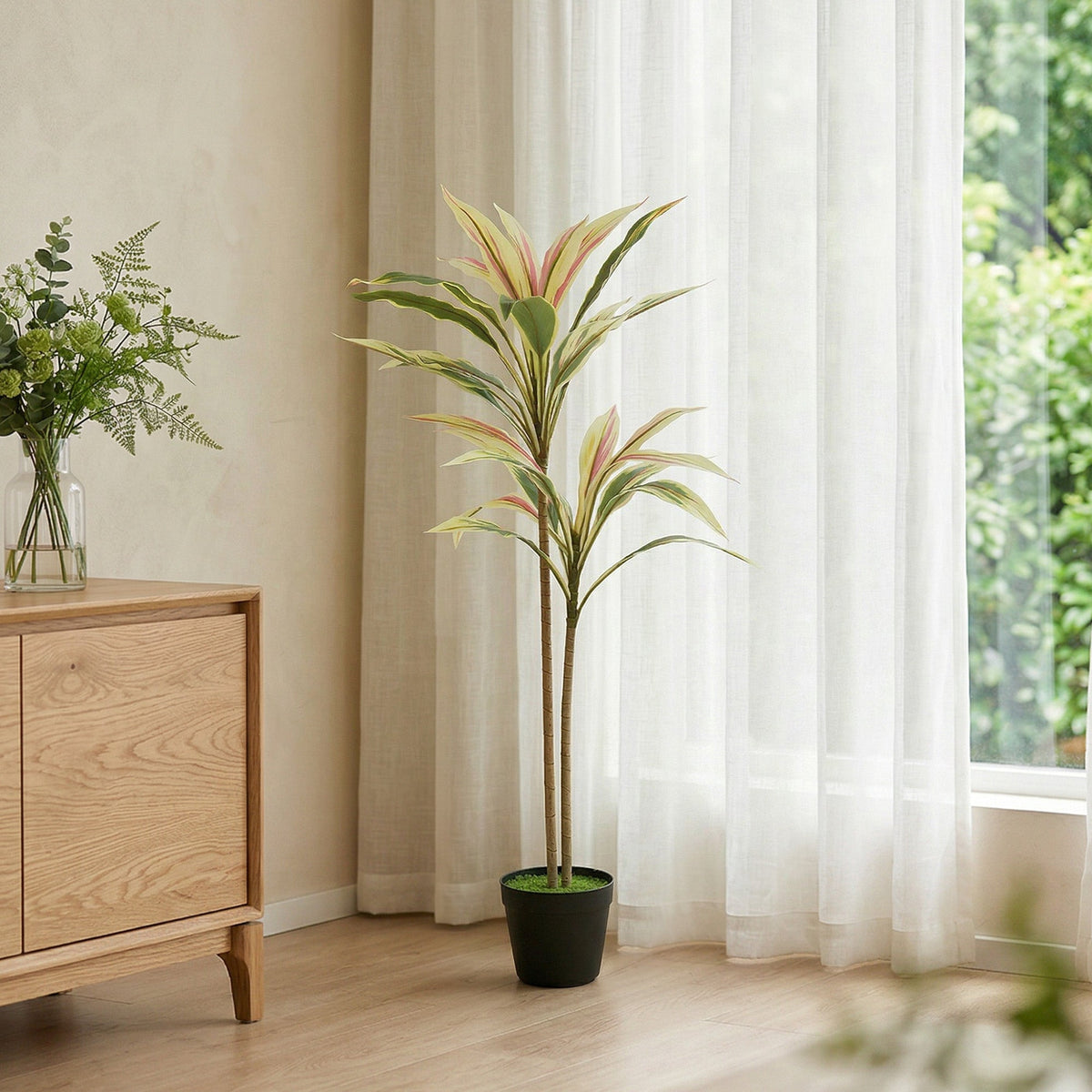 Artificial cordyline tree in a black pot by a window with sheer curtains in a bright room