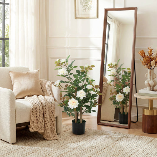 The artificial plant standing in a bright living room next to a tall wooden floor mirror