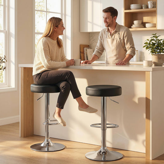Two black PU leather swivel bar stools with chrome bases and footrests in a modern kitchen setting