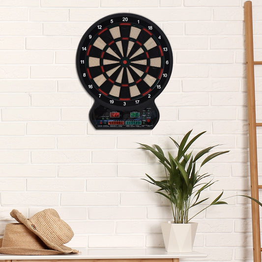 The electronic dartboard mounted on a white brick wall above a table with a plant