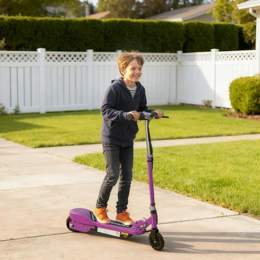 A smiling boy rides the purple kids electric scooter down a paved path outdoors